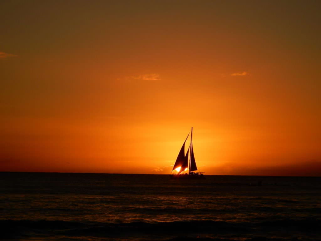 Single sailboat at Waikiki sunset, orange and black